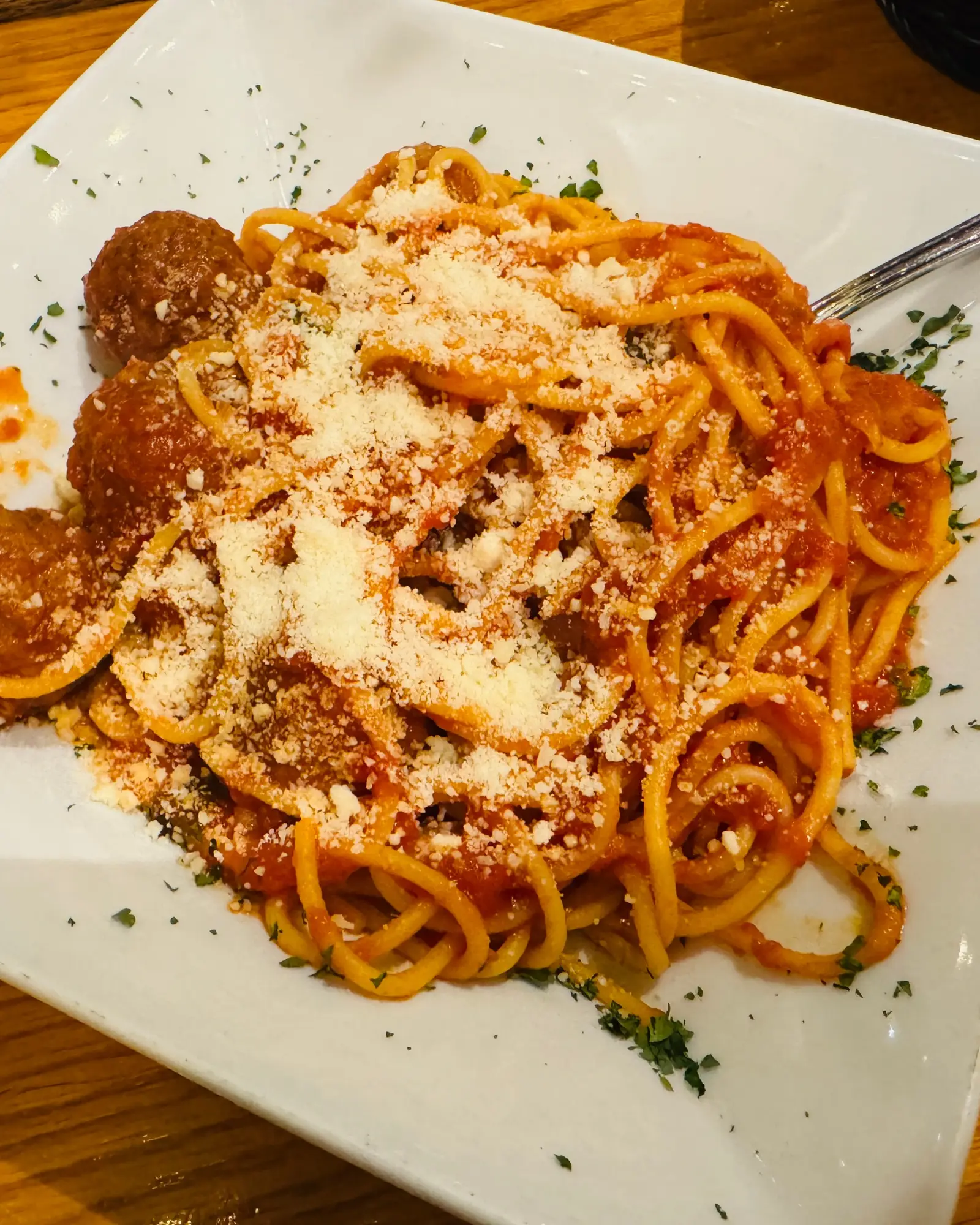Espaguete ao sugo com almôndegas e parmesão ralado, servido em prato branco