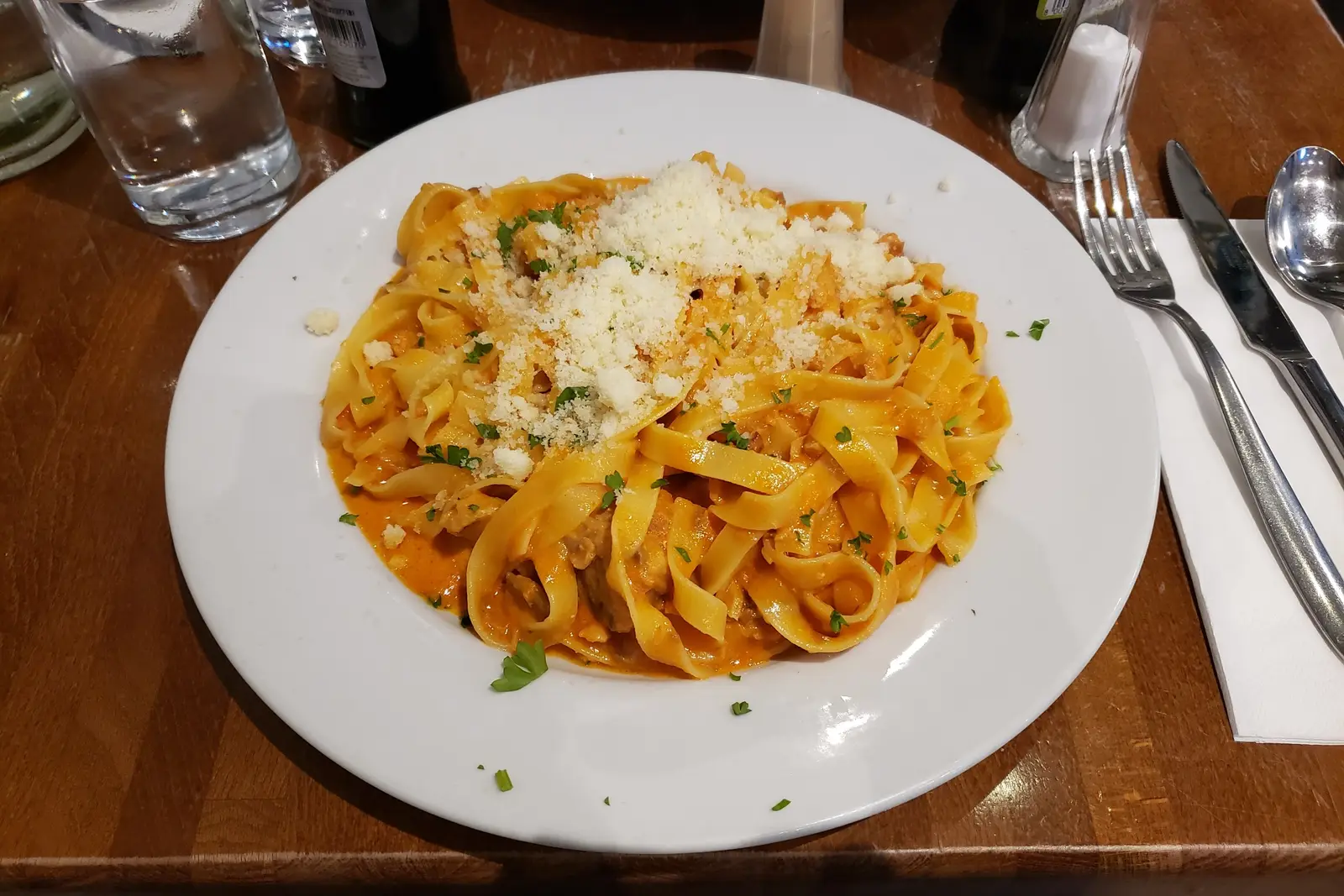 Prato de tagliatelle ao molho rosé com parmesão ralado, sobre mesa de madeira