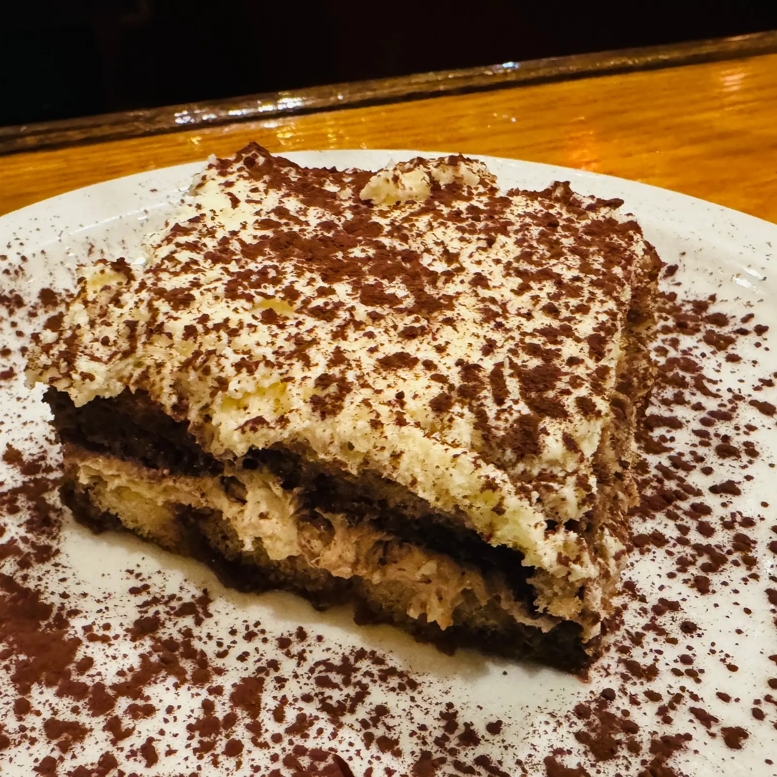 Fatia de tiramisù polvilhada com cacau, em prato branco