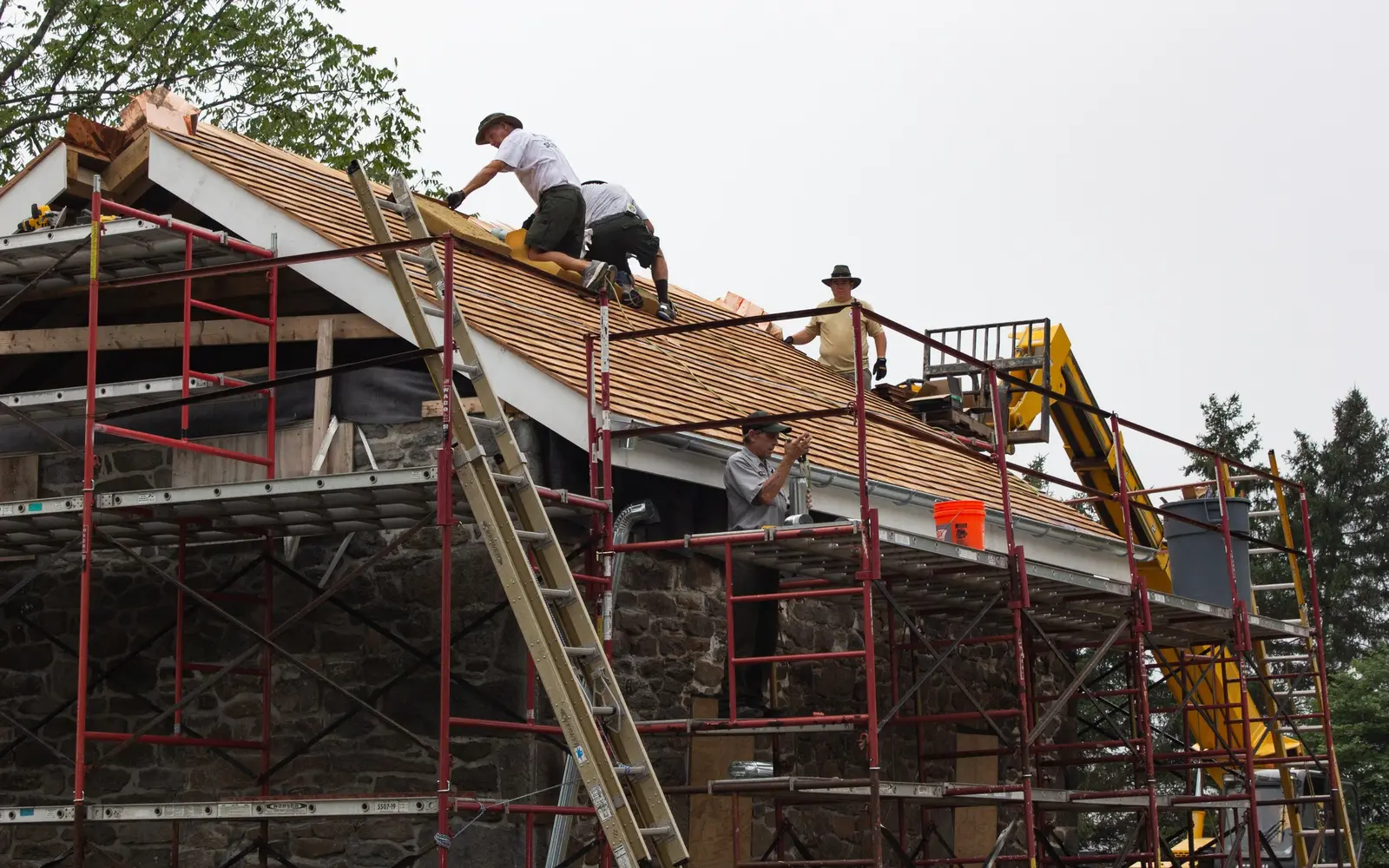 Roofing crew nailing new wood shingles on a steep roof, with scaffolding along the eaves
