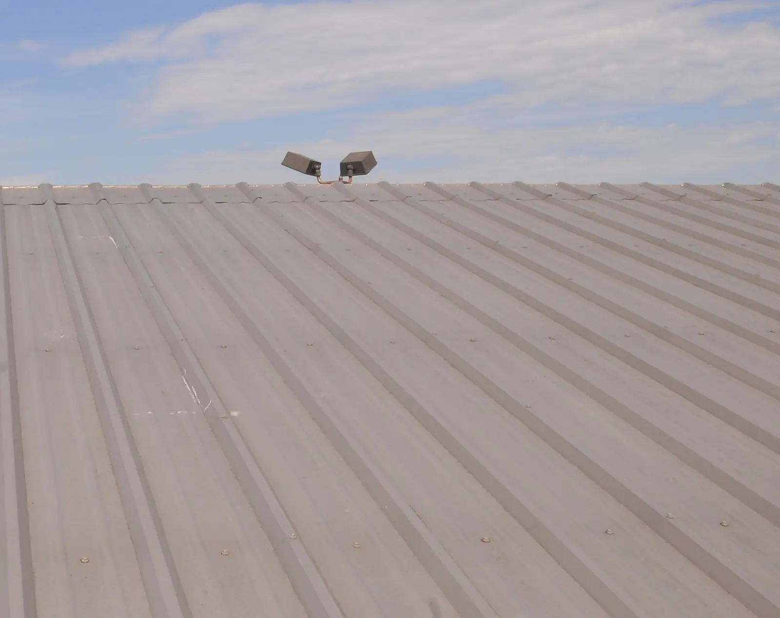 Metal roof panels under a blue sky, photographed during a hail damage inspection